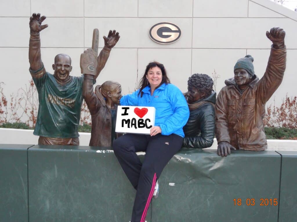 Church member holding an I Love MABC sign among the statues at Lambeau Field, Green Bay