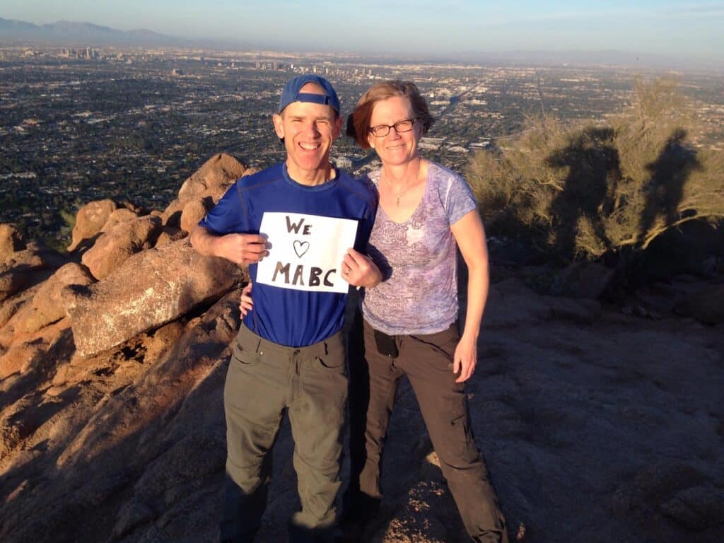 Two church members holding a We Love MABC sign on a hilltop above Phoenix, Arizona